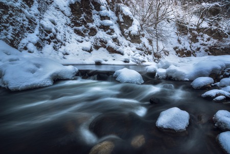 Slow flowing water. River snow bank on a winter forestの写真素材