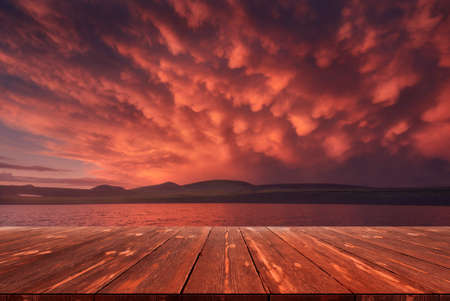 After the storm. Beautiful red clouds over the lake after rain with empty wooden table. natural template landscape.の写真素材
