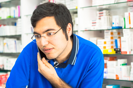 Eskisehir, Turkey - June 14, 2017: Portrait of young male pharmacist talking on the phone at counter in the pharmacy.のeditorial素材