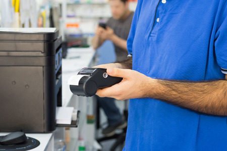 Detail of pharmacist hands holding a card reader at the counter in the pharmacy