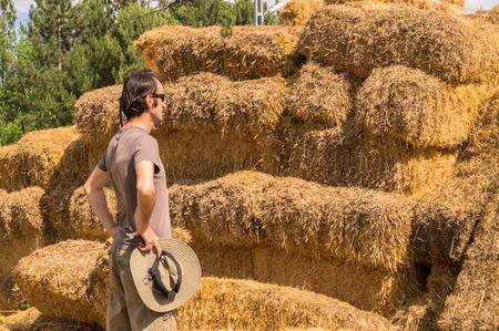 Handsome guy with hat standing with hands on his waist near straw bales.の写真素材