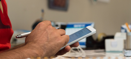 Close up of a young man hand using mobile smart phone in the office. Man holding a pen in his hand.