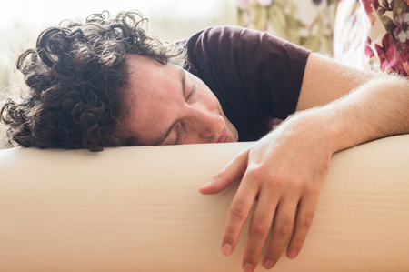 Young handsome man with curly hair sleeping on the sofaの写真素材