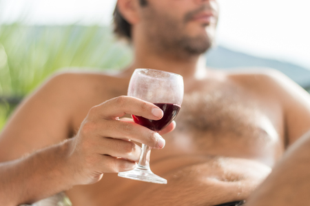 Young relaxed Caucasian man holding a dirty glass of red wine in the balconyの写真素材