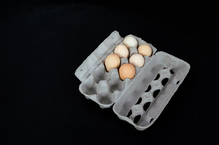 Cardboard egg box with six eggs on black felt background.の写真素材