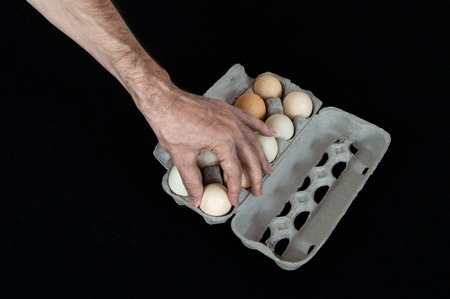 Male hand taking one egg from cardboard egg box on black felt background.