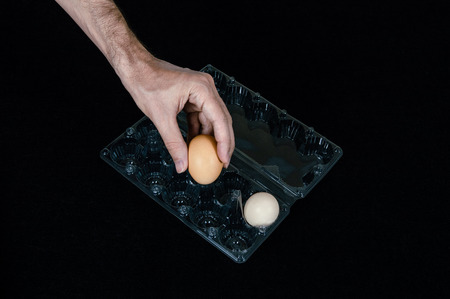 Male hand taking one egg from plastic egg box on black felt background.