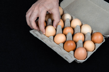 Male hand taking one egg from cardboard egg box on black felt background.