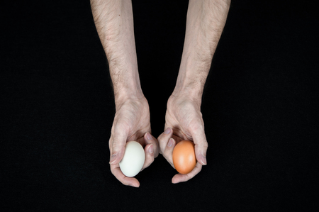 Man holding one white egg in his hand, and one brown egg in his other handの写真素材