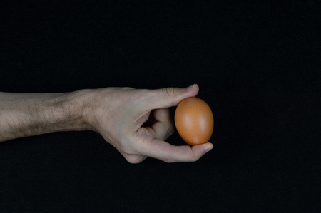Man holding a brown egg with his fingers on a black felt background