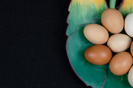 Top view of hen eggs in a leaf shaped plate and on a black background.