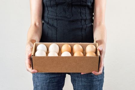 Caucasian woman with black shirt holding a cardboard egg box full of hen eggs on a white background.の写真素材