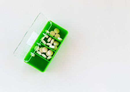 Top view of white medical tablets in an opened green medication box on white background. Medication concept.の写真素材