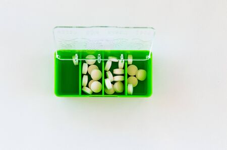 Top view of white medical tablets in an opened green medication box on white background. Medication concept.の写真素材