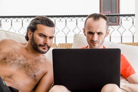 Two men working remotely from home on laptop in a balcony on a sunny day. Freelancing concept.
