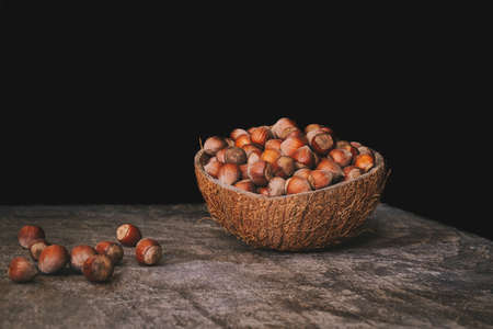 Pile of shelled hazelnuts in a coconut shell bowl on a wooden table on black background. Healthy eating.の写真素材