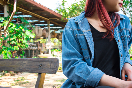 Women wear black t-shirt and blue shirt. Sit on a wooden chair facing left. Thailand, Asiaの写真素材