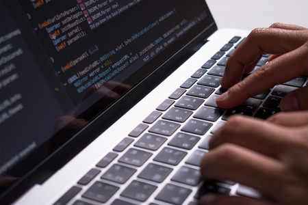Close up. The developer's hand is creating code on a computer monitor on a white desk.の写真素材