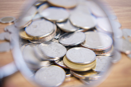Image of many coins through a magnifying glass lying on a wooden table.の写真素材