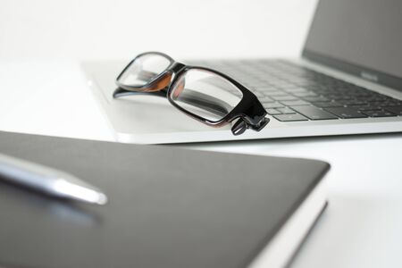 Close-up of eye glasses on a computer on a modern table in white With pen and notebook.