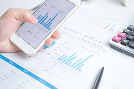 Smart phone screen shows a graph of the financial business desk white.の写真素材