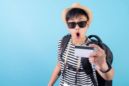 A young Asian man is happy to take a credit card and travel.Isolated on a blue background.