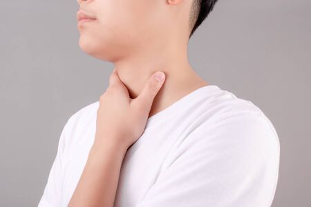 Asian people wear white T-shirts, using their hands to touch the neck. On a gray background. Sore throat.  Health and medical care concept.の写真素材