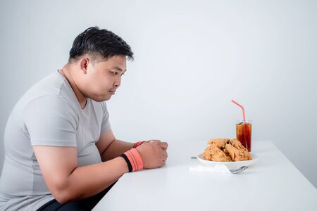 Overweight young man looking at fried food on a white table. Which he is hungry after exercisingの写真素材