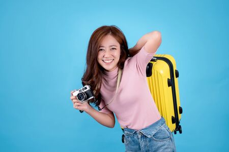 Beautiful Asian tourists carrying yellow suitcases. She is excited to travel on a blue background. In the studioの写真素材