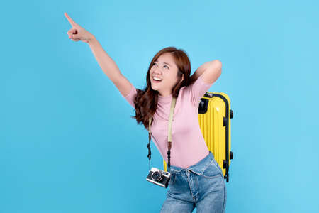 Beautiful Asian woman is smiling, carrying a yellow suitcase and pointing to an empty space by hand...