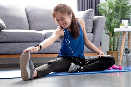 Beautiful Asian women warm up before exercising at home. She is listening to music from her...