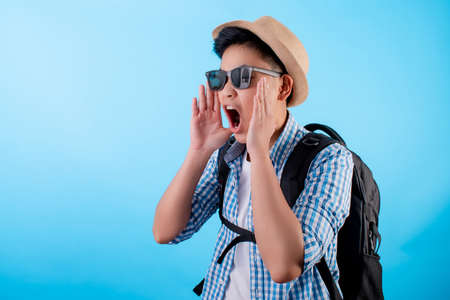 Happy Asian Backpackers. He is shouting open mouth for the copy space on a blue background.