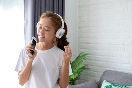 Asian women are listening to music and she sings in the room happily.