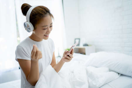 Young women listening to music and singing in the room. She listens to her favorite songs using the app on her phone.の写真素材