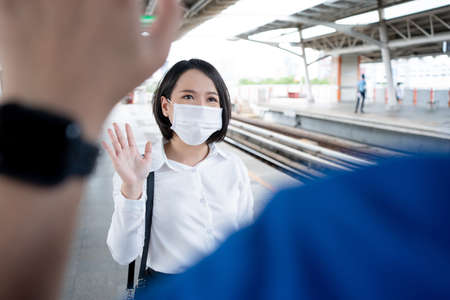 Young Asian woman wears a mask and greets a friend on a subway train in big city at Covid19 outbreak, social distancing and new normal concept.の写真素材