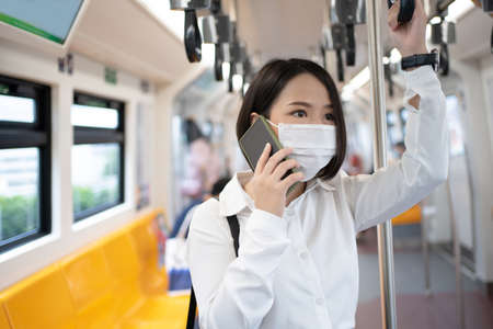 A young Asian businessman in a mask uses a phone in the subway while there is an outbreak of...