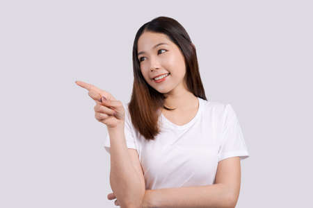 Beautiful asian woman pointing to promotional design copy space, isolated on white background.の写真素材