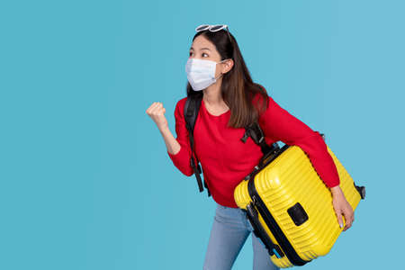 Young traveler wearing a mask carrying a suitcase on vacation.の写真素材