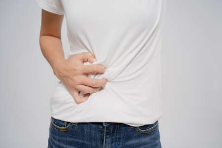 Pain in a waman's body. Asian woman has a stomachache on a white background. She holds her belly with her hands.の写真素材