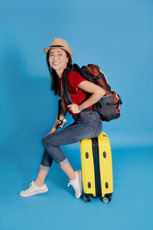Young Asian traveler sitting on a yellow suitcase. She is smiling and ready to travel on vacation.の写真素材
