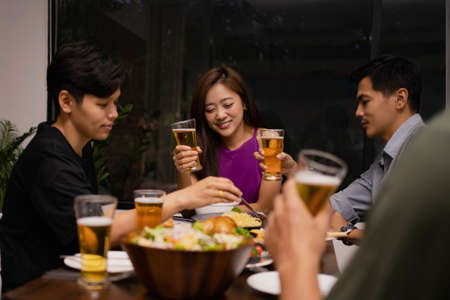 Working group of young Asians drinking beer and clink glasses in a restaurant. They're relaxed.の写真素材