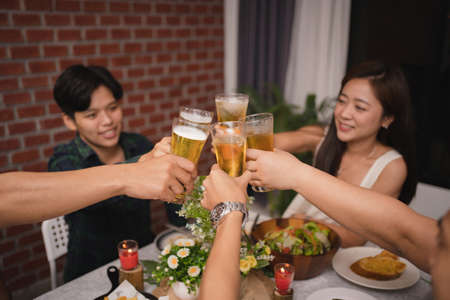 Group of Asian friends had a party at home in the evening. They are eating and drinking beer.の写真素材