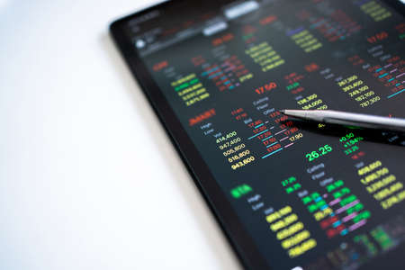 Pens pointing at the stock market trader's numbers on a tablet screen on a white table. Trading on...