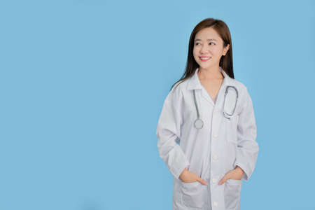 Portrait of a beautiful Asian female doctor is smiling.  She stands is isolated on blue background.の写真素材