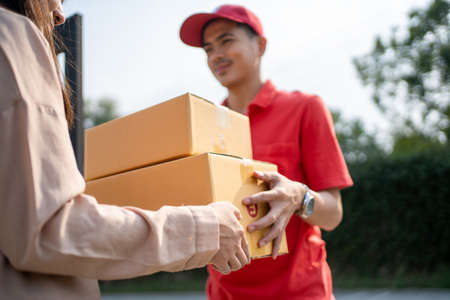 The postman delivered the parcel home with a smile and a happy face. Young Asian woman taking a box from the postman at the door.の写真素材
