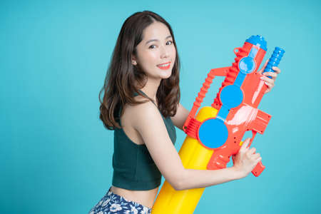 Smiling Asian woman stands sideways holding a water gun for Songkran festival isolated on a blue...