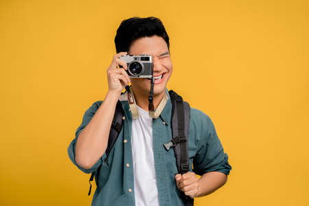 Portrait of a young backpacker Asian tourist taking a picture on a yellow background. He is very happy.の写真素材