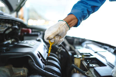 Young car mechanic checks the engine oil. Car service and maintenance concept.の写真素材