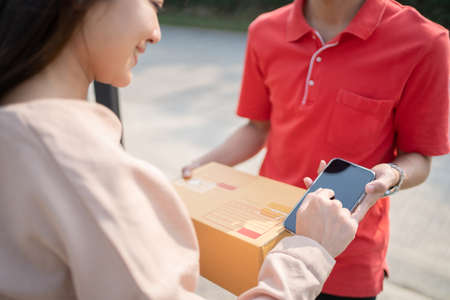 A smiling Asian woman receiving a package from a delivery man at home.の写真素材