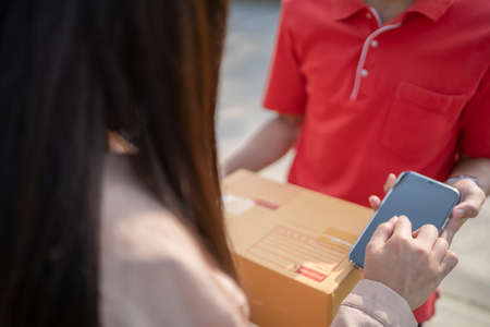 Young woman is writing a signature on a digital phone after receiving a parcel from delivery man.